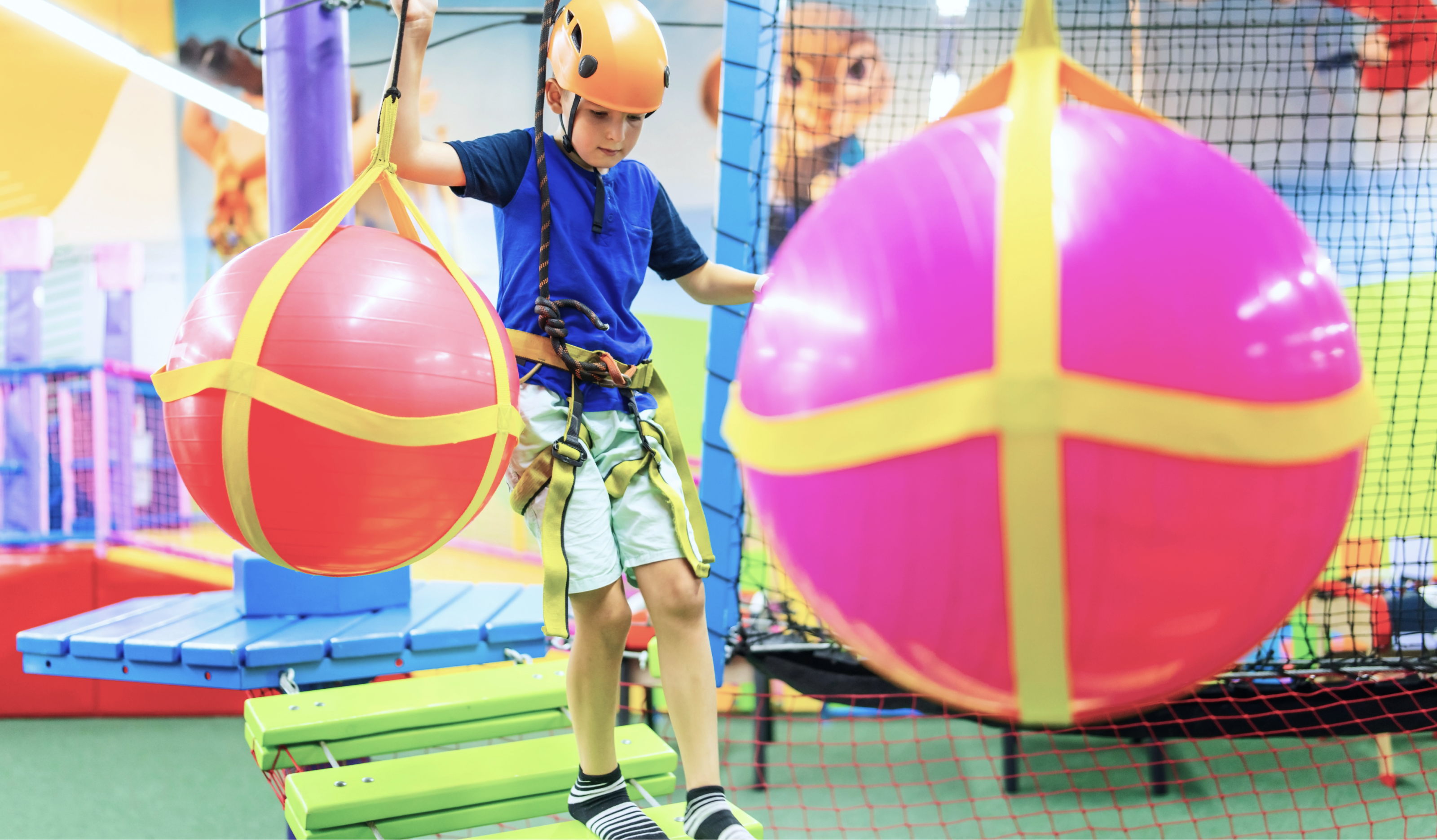 A young boy walking across a bridge at an obstacle course with a harness and a helmet